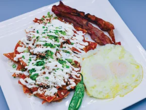 Chilaquiles served with queso fresco, green onions and sour cream. Served with eggs and bacon.
