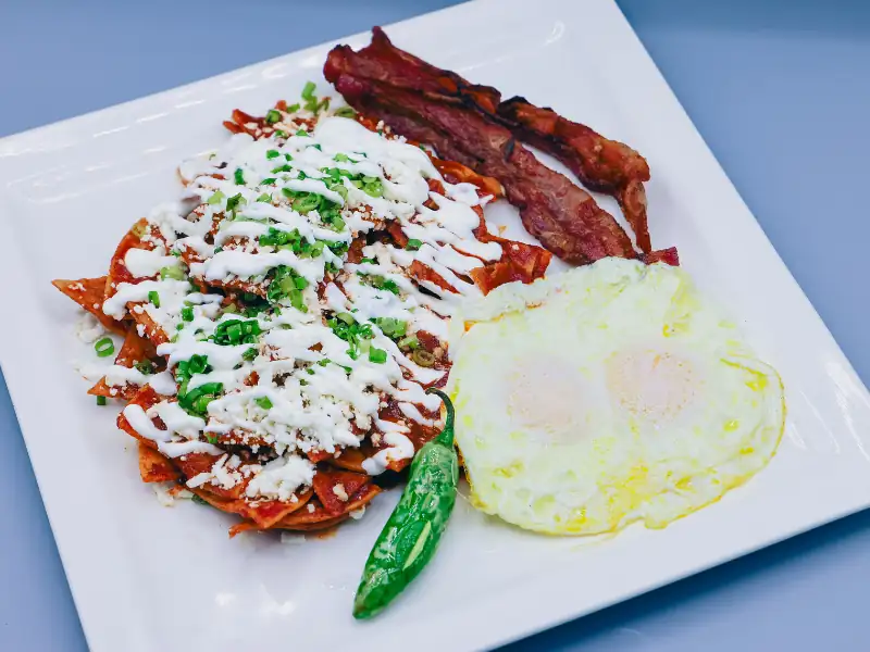 Chips tossed in red sauce then topped with crema, queso and green onions. Served with bacon and eggs.