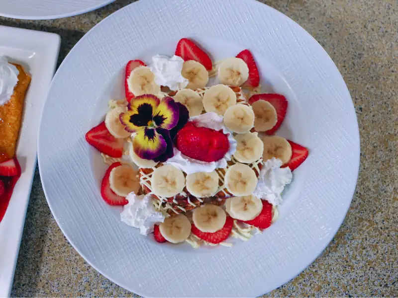 Two French toast slices stuffed with cream cheese. Topped with banana slices, strawberry slices and whipped cream.